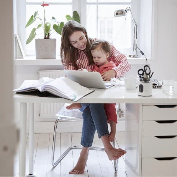 Woman sitting at desk working while holding a toddler in her lap.