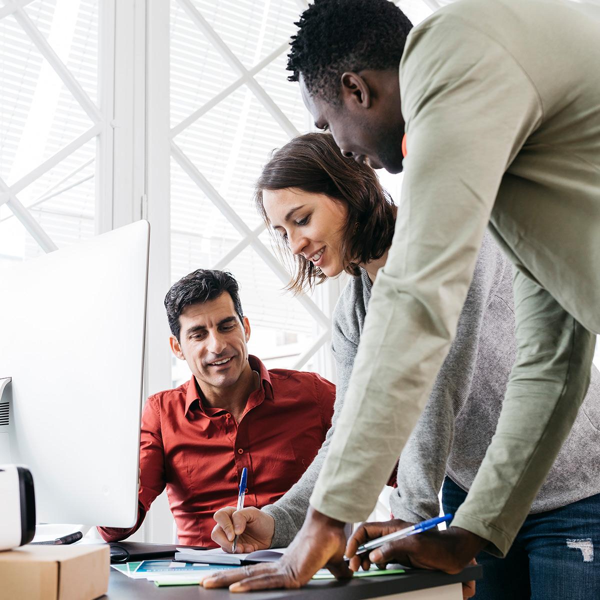 3 co-workers on a computer writing answers on a pad.