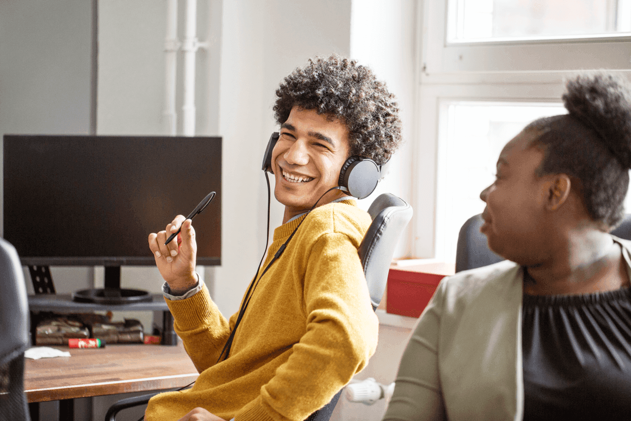 Smiling business colleagues working together in office. Male professional wearing headphones smiling with female colleague in office.