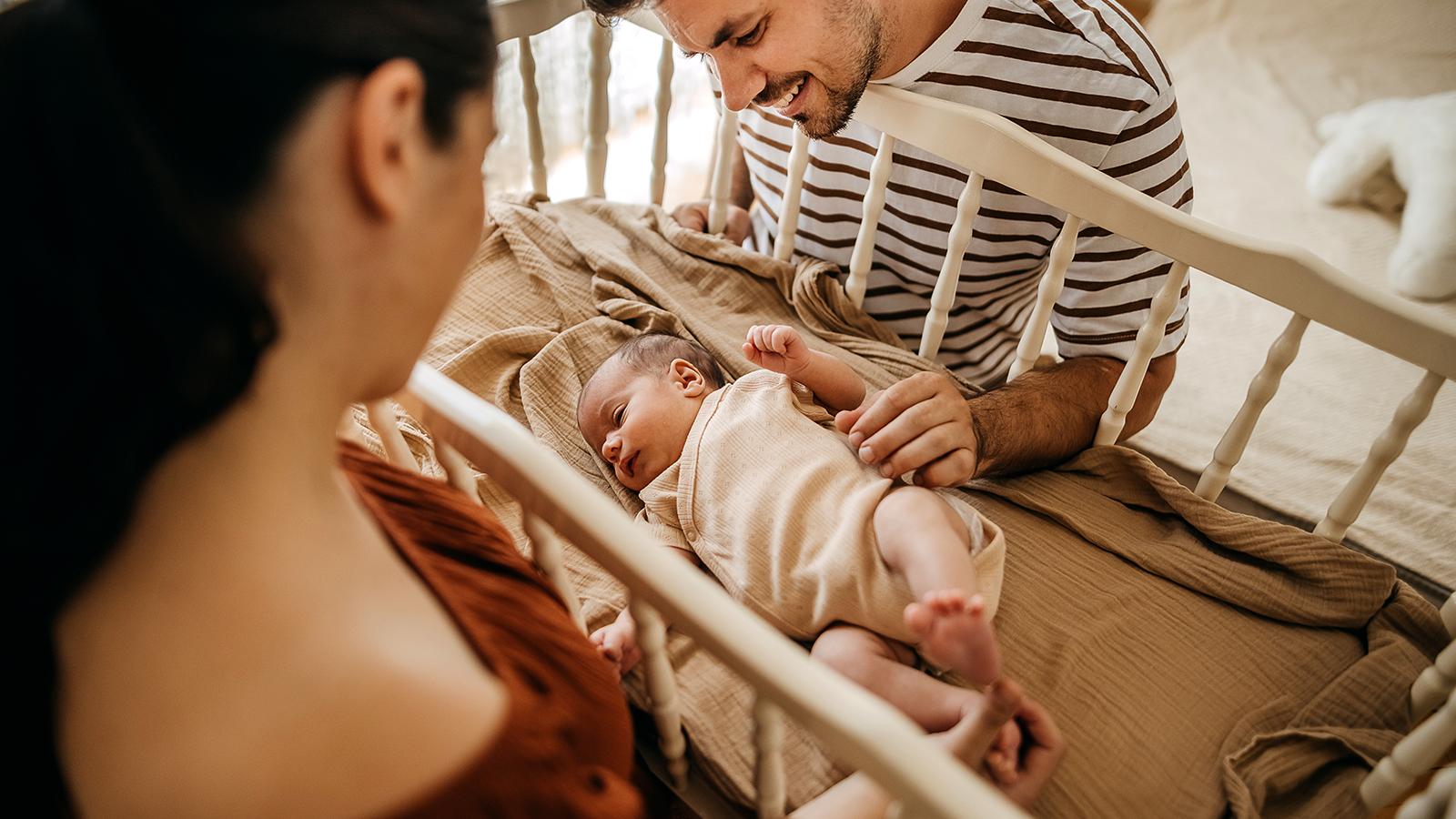 A mother and father looking at their baby in a crib
