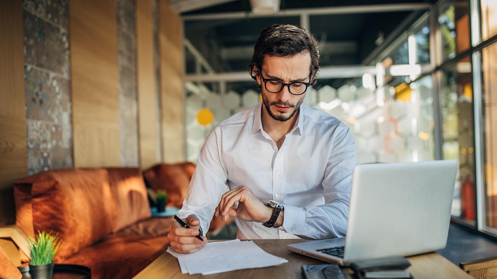 Man wearing glasses looking at his watch at his desk
