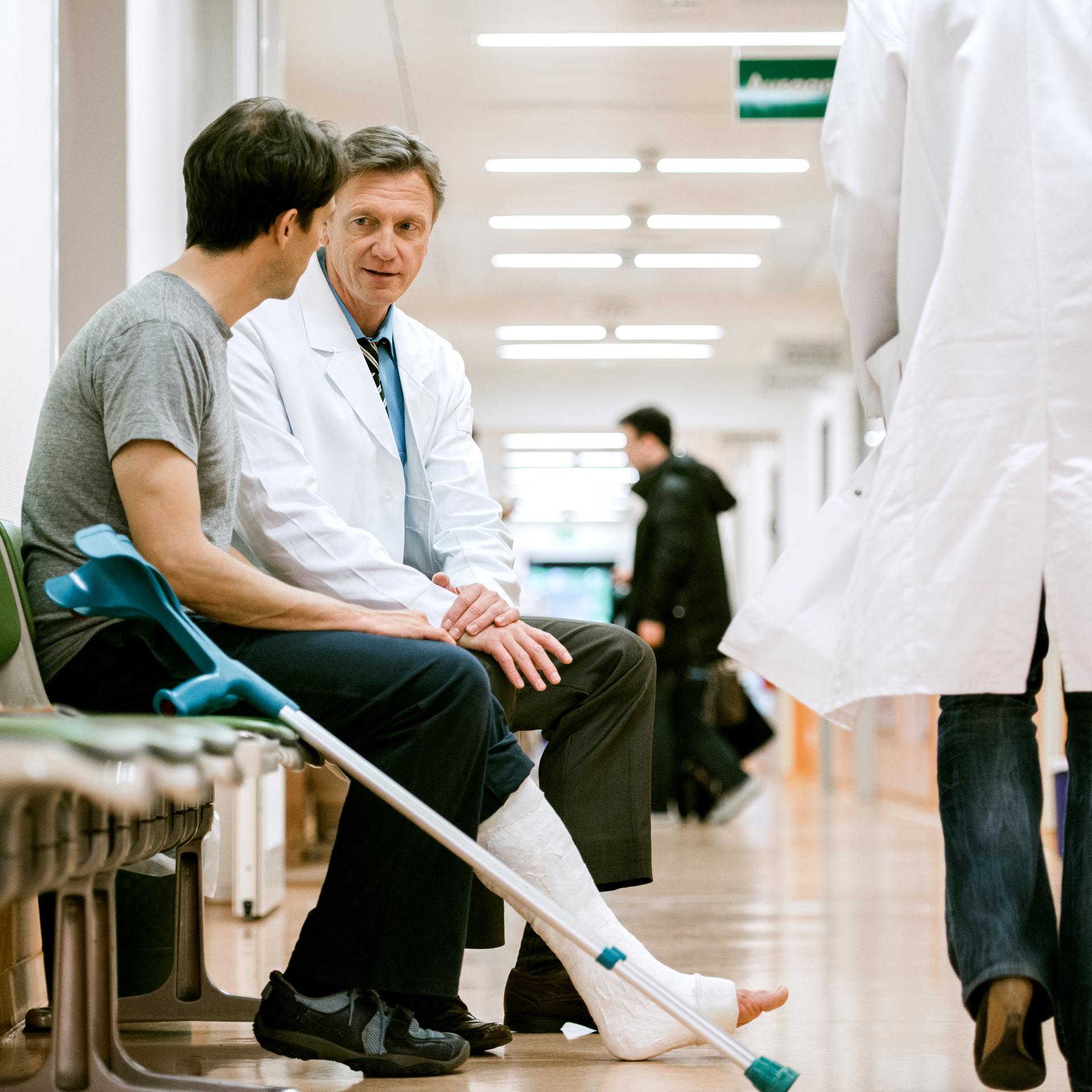 Man with a leg cast and crutches talking to a doctor.
