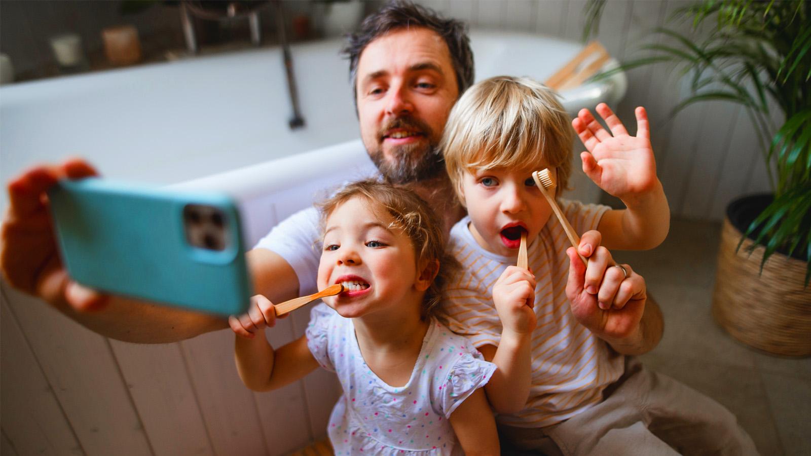 Dad taking a selfie with his two children while they hold tooth brushes