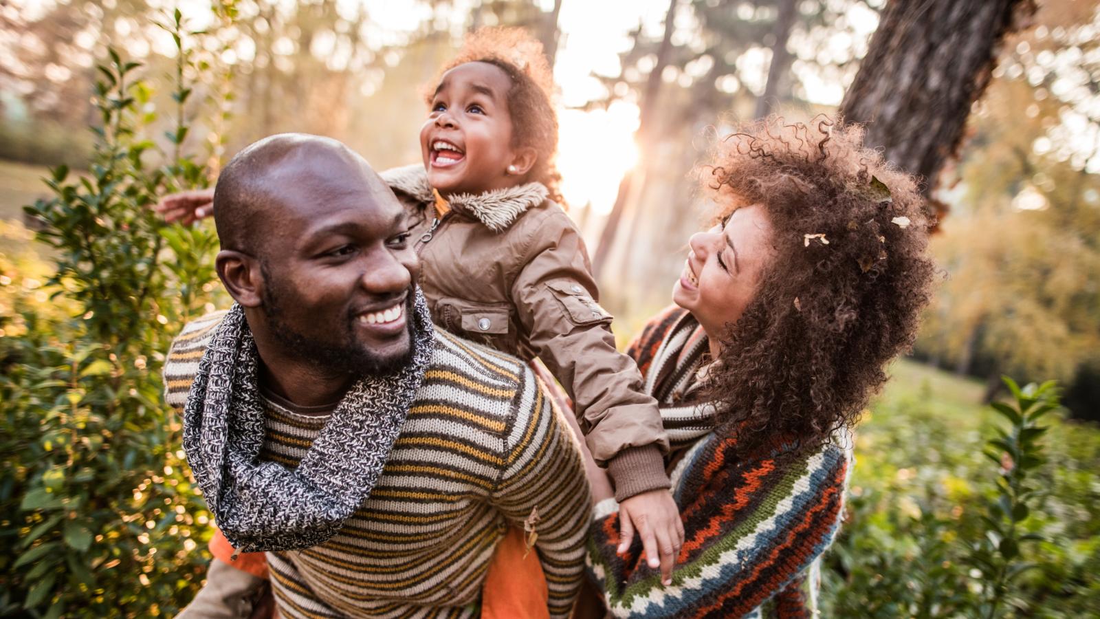 Young daughter riding the back of her father with her mother holding her Young daughter riding the back of her father with her mother holding her