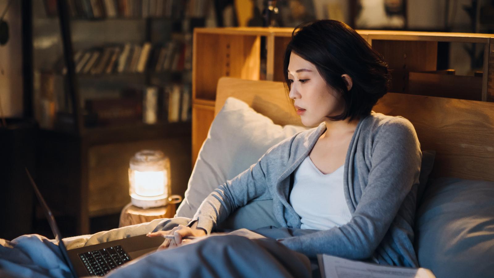 Woman working on her laptop at night in her bed