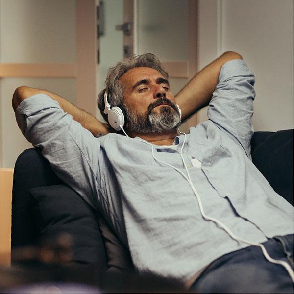 Man with his hands behind his head listening to music on his couch.