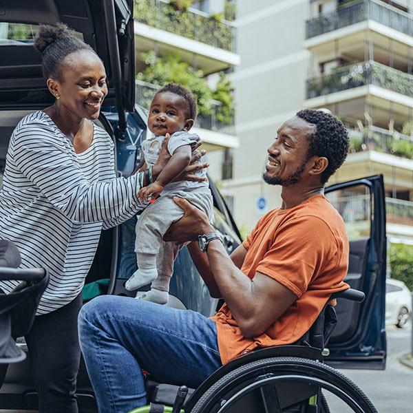 A man in a wheelchair hands a baby to a woman..