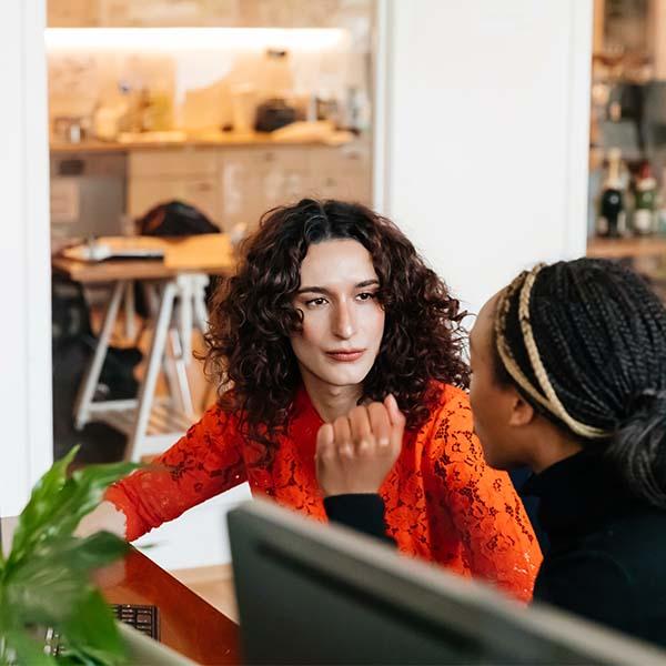 Transgender employee in modern office talking with colleague.