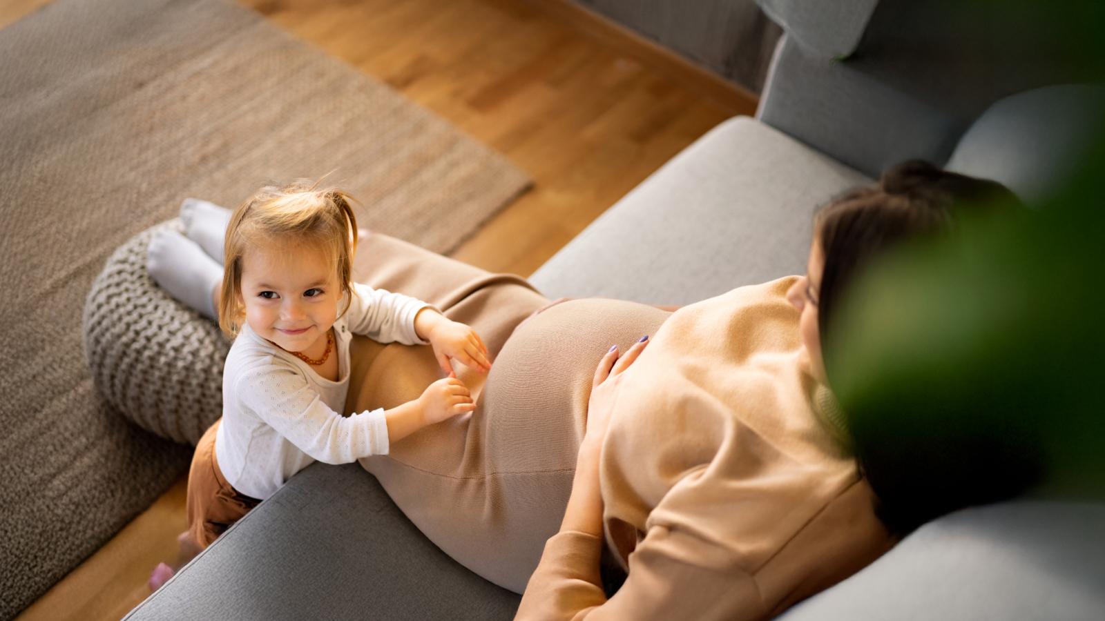 Pregnant woman sitting down with her toddler next to her.