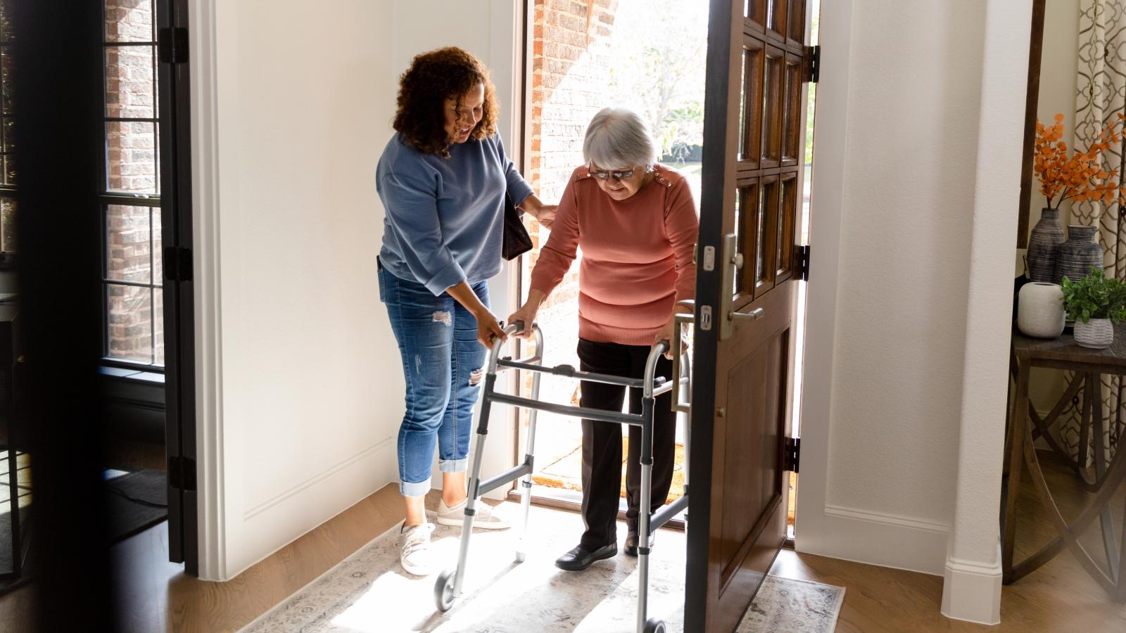 Younger woman helping an older woman get into her home