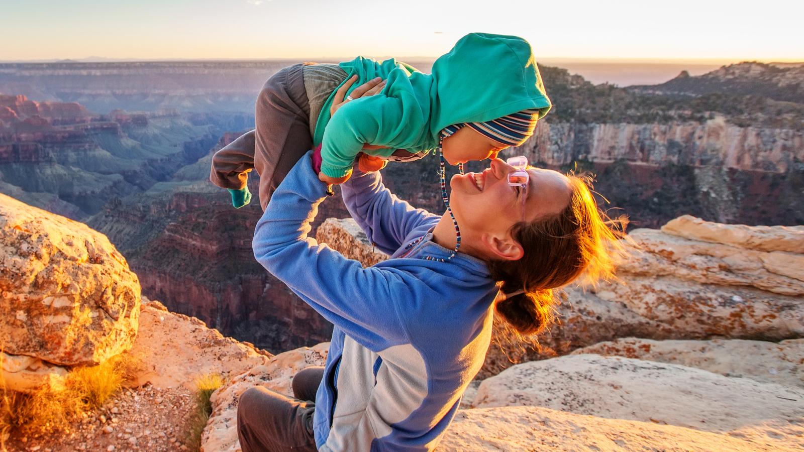 Mother holding her baby up while in the mountains