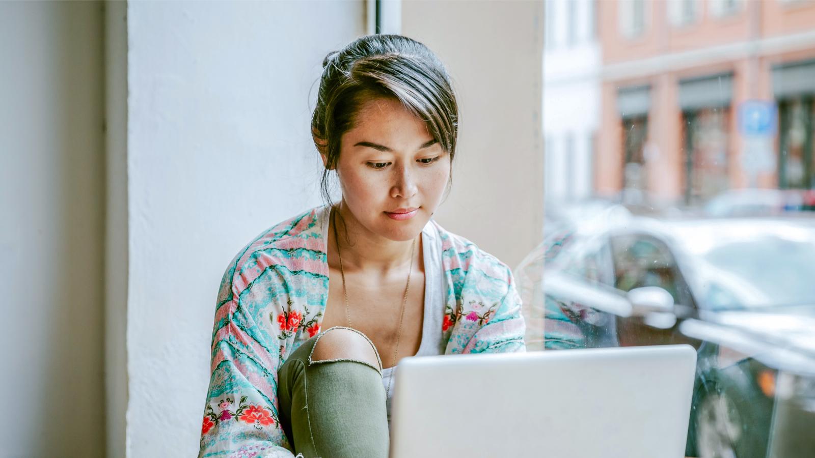 Young woman working on laptop in cafe window