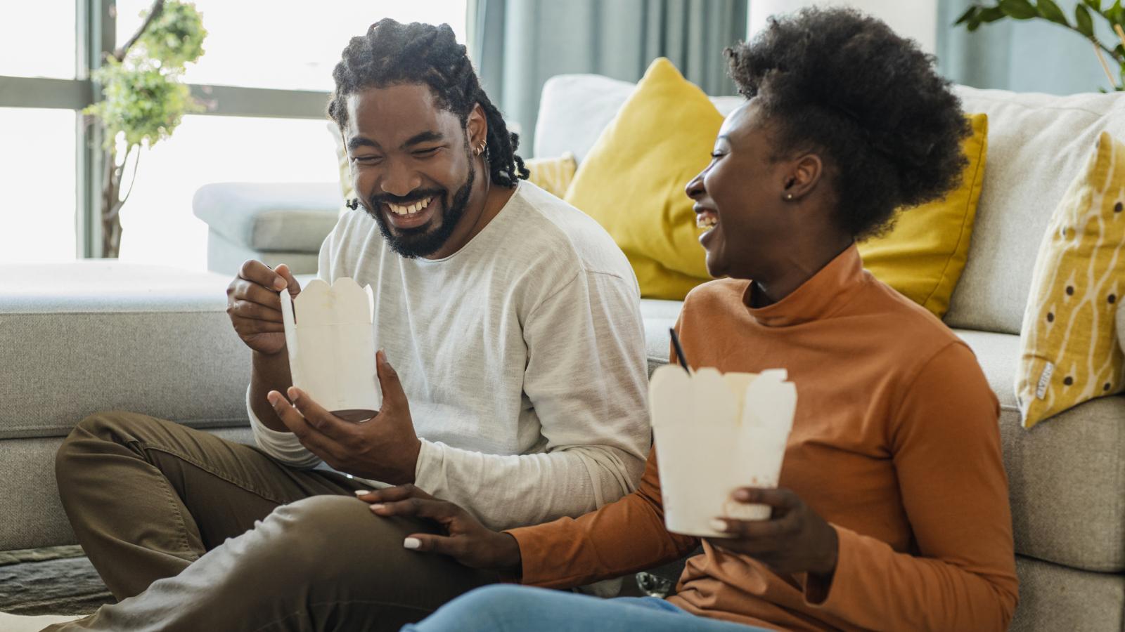 Couple laughing together while eating takeout food. Couple laughing together while eating takeout food.