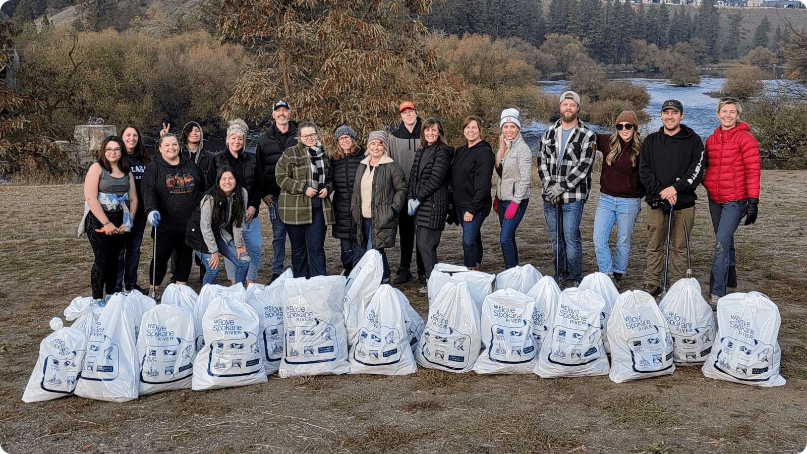 A large group of Guardian colleagues stand in a line beside a river, showing off a row of trash bags they filled with trash from the riverside A large group of Guardian colleagues stand in a line beside a river, showing off a row of trash bags they filled with trash from the riverside