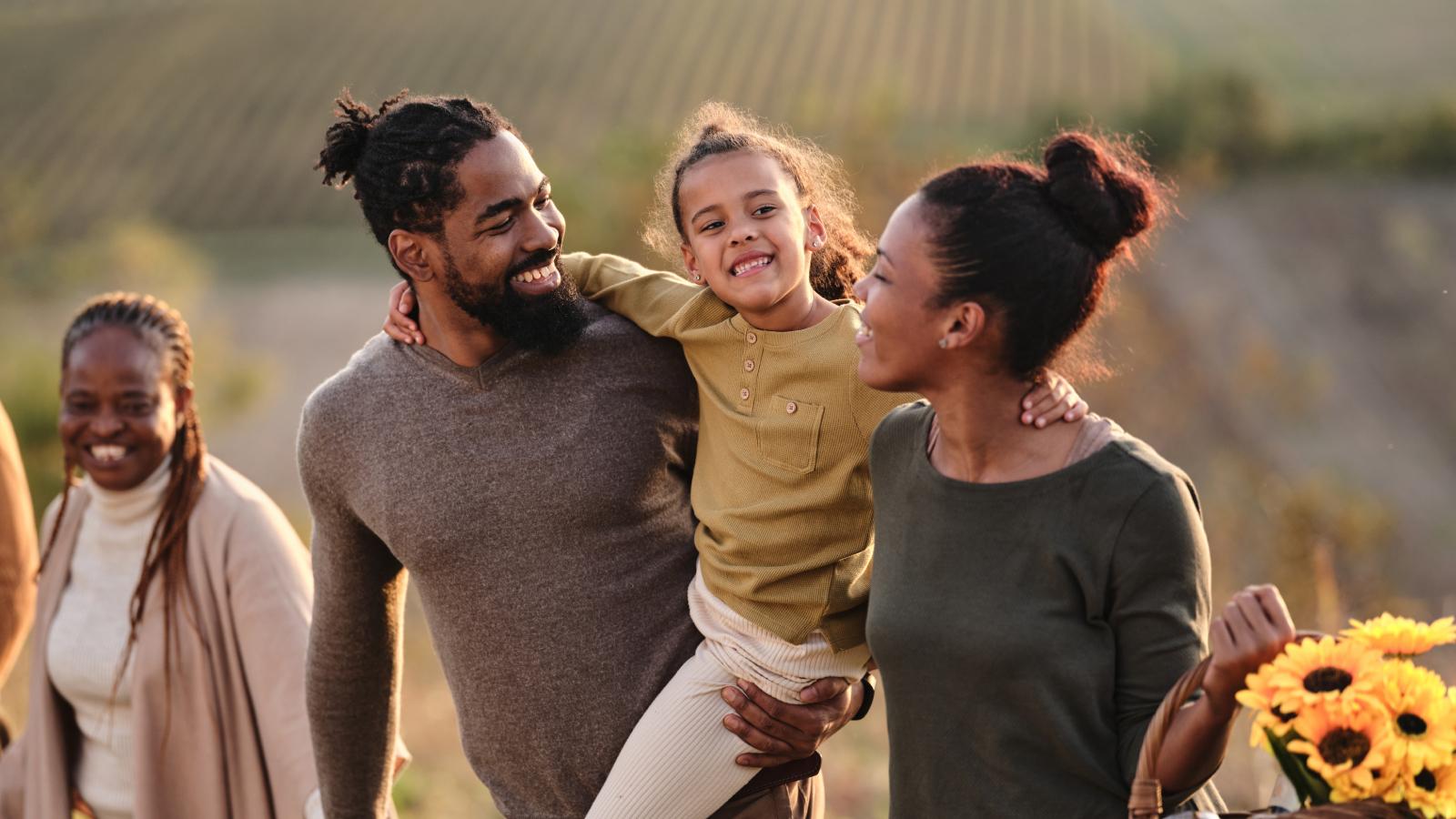 smiling mother and father carrying young daughter through field