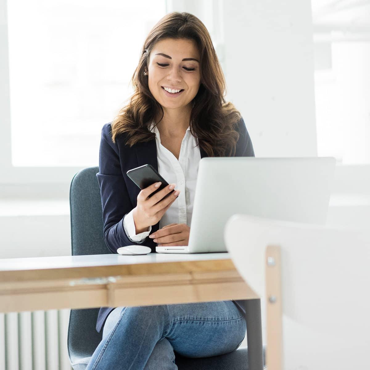 Woman on her phone while sitting at her desk.