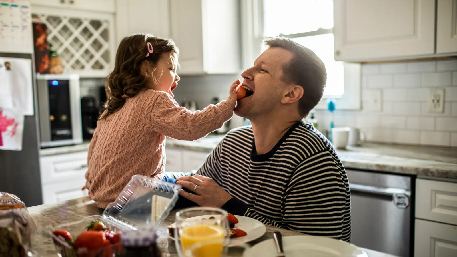Father eating strawberries in the kitchen with his daughter. Father eating strawberries in the kitchen with his daughter.