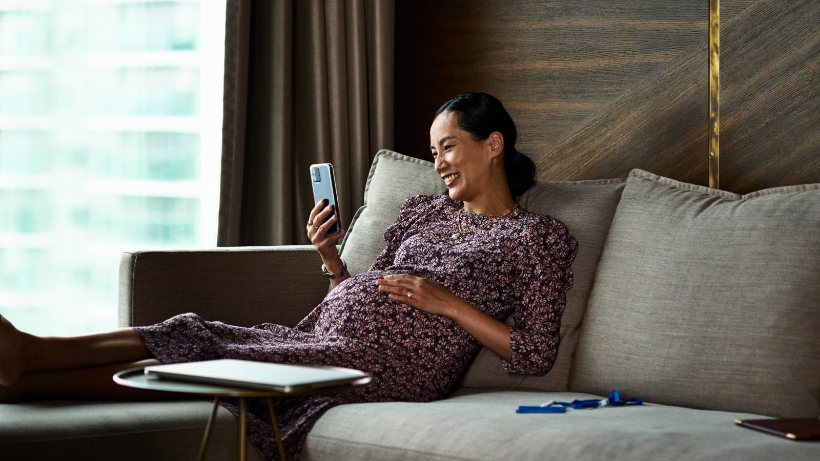 Pregnant woman sitting on a couch and looking at her phone. Pregnant woman sitting on a couch and looking at her phone.