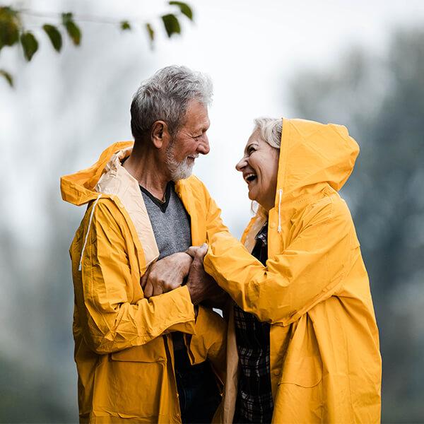 Happy senior couple in raincoats talking in the rain.