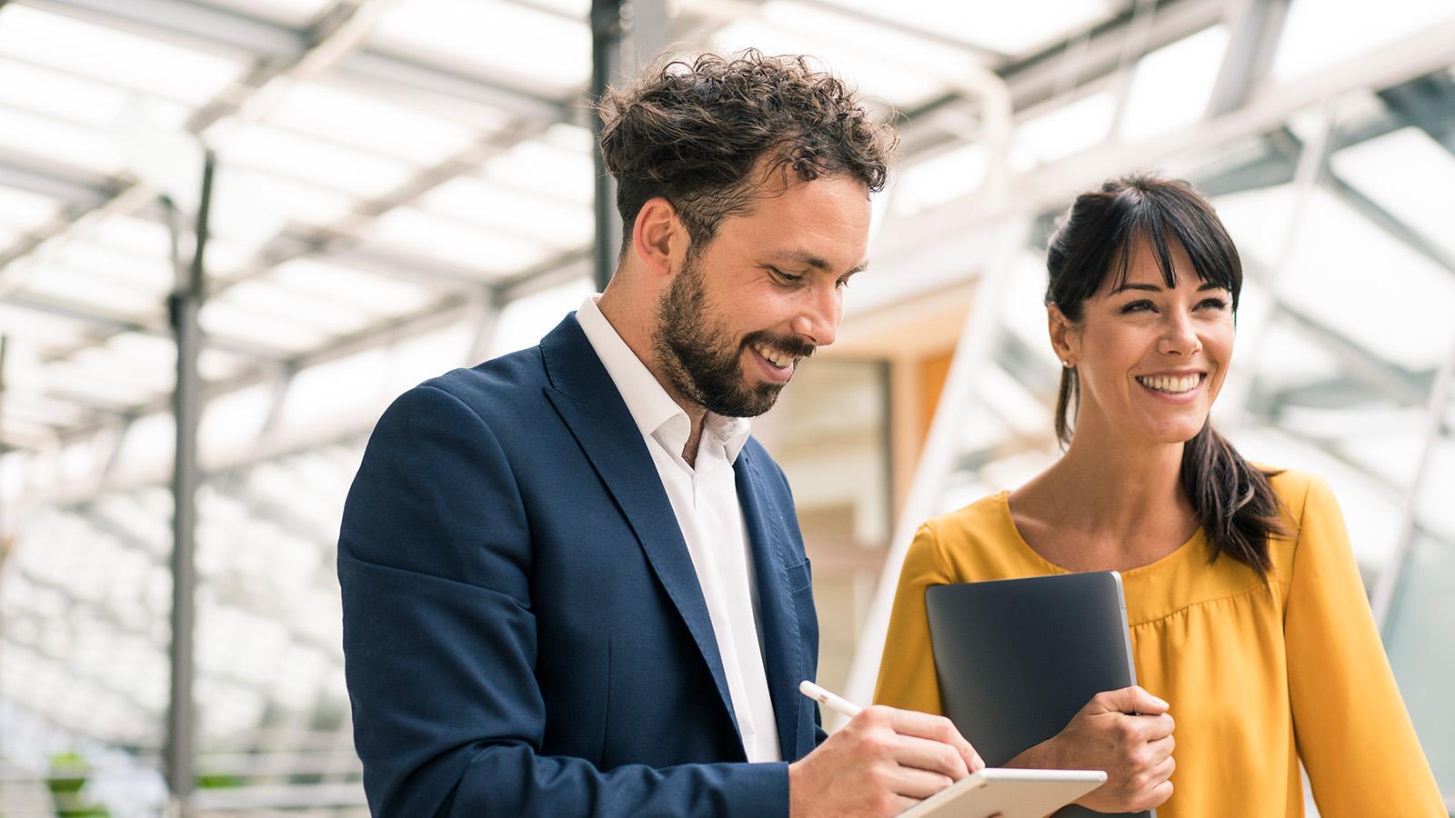 Man and woman walking through an office holding notebooks