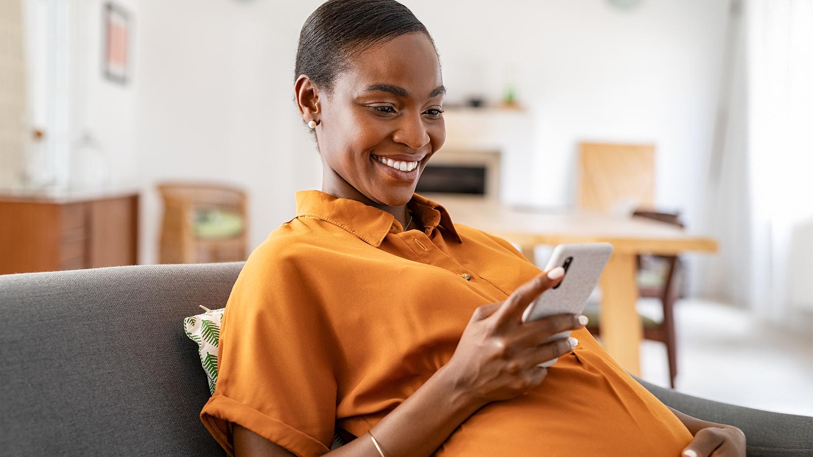 Pregnant woman sitting on a couch looking at her phone