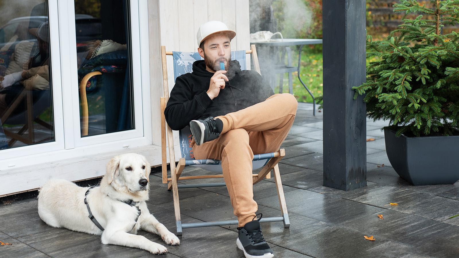 Man smoking a vape pen sitting outside with his dog.