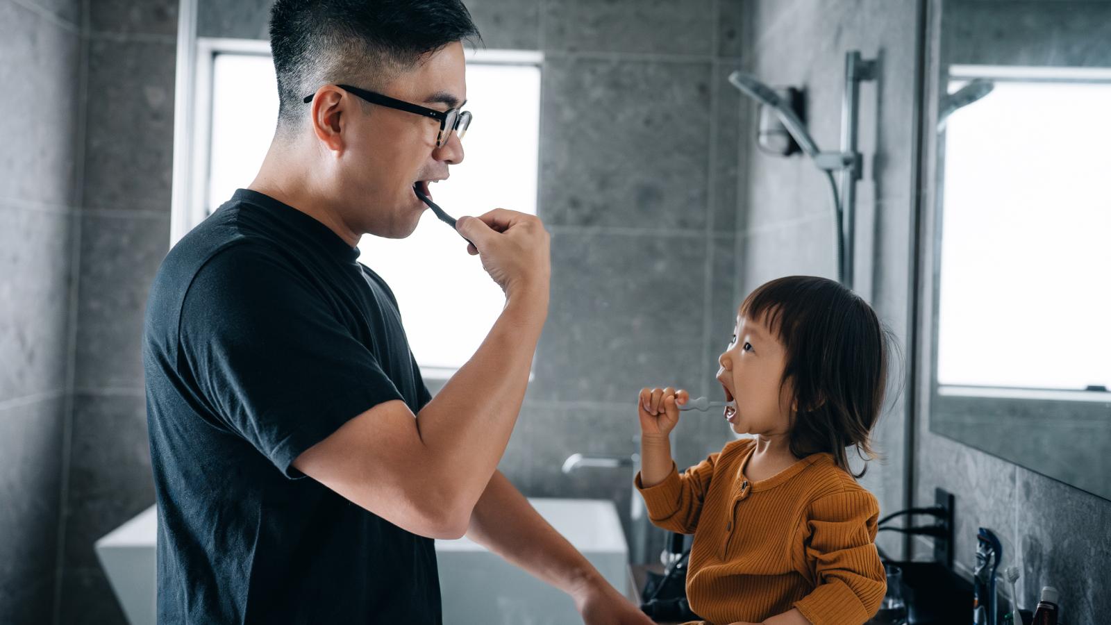 Father and daughter brushing teeth together