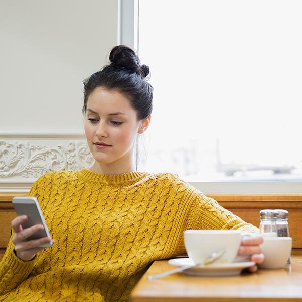 Woman sits in coffee shop reading on her phone.