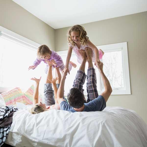 Two kids play airplane with their parents on a bed..