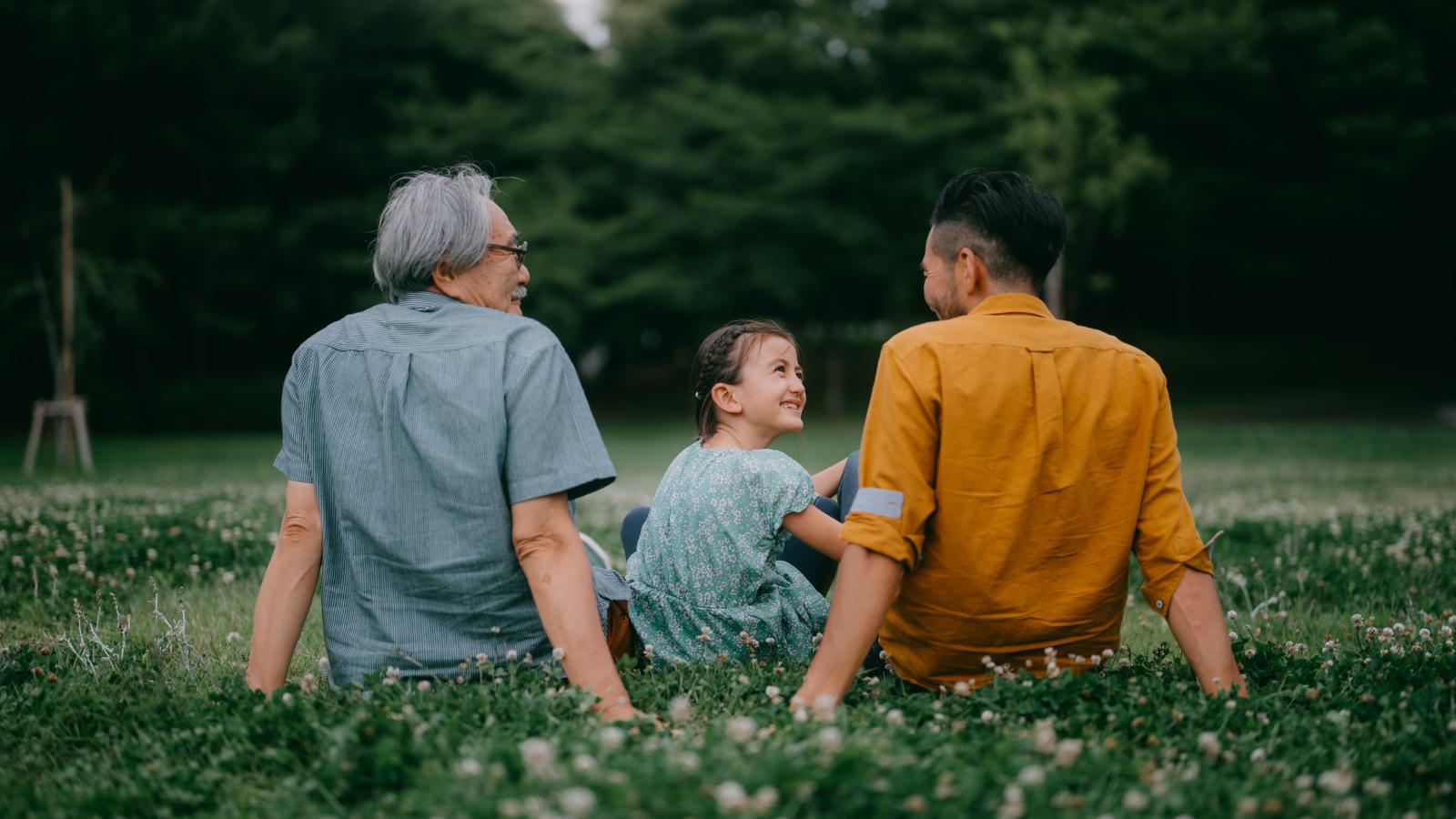 Three generation family sitting on grass in a park.