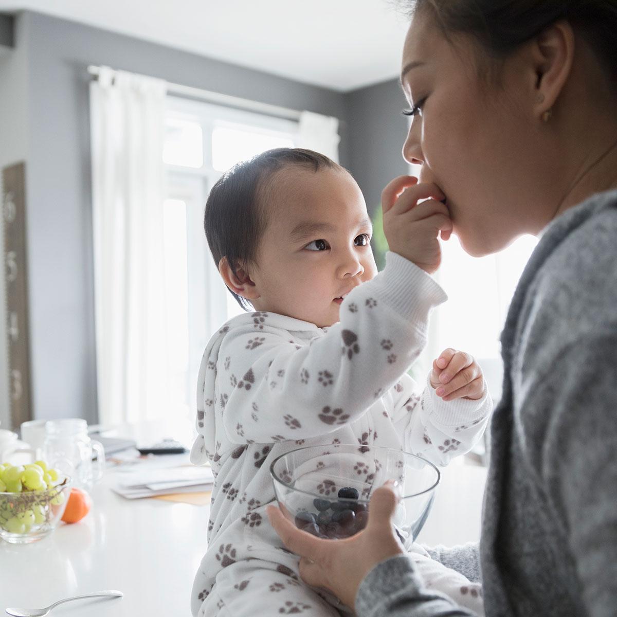 Baby sitting down feeding her mom food.