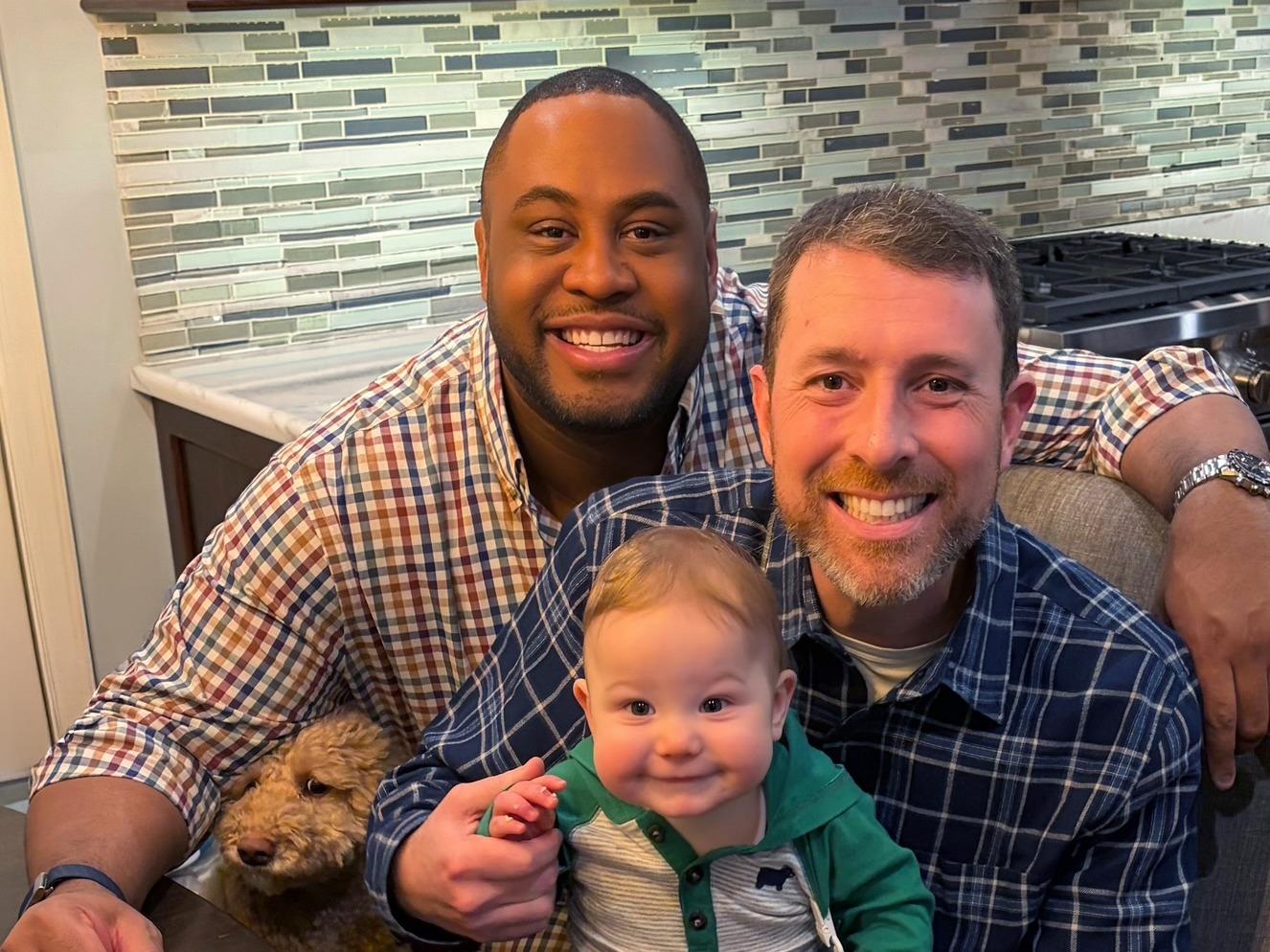 AR25 - Colleague story img Two men smile at the camera with their baby boy and dog.