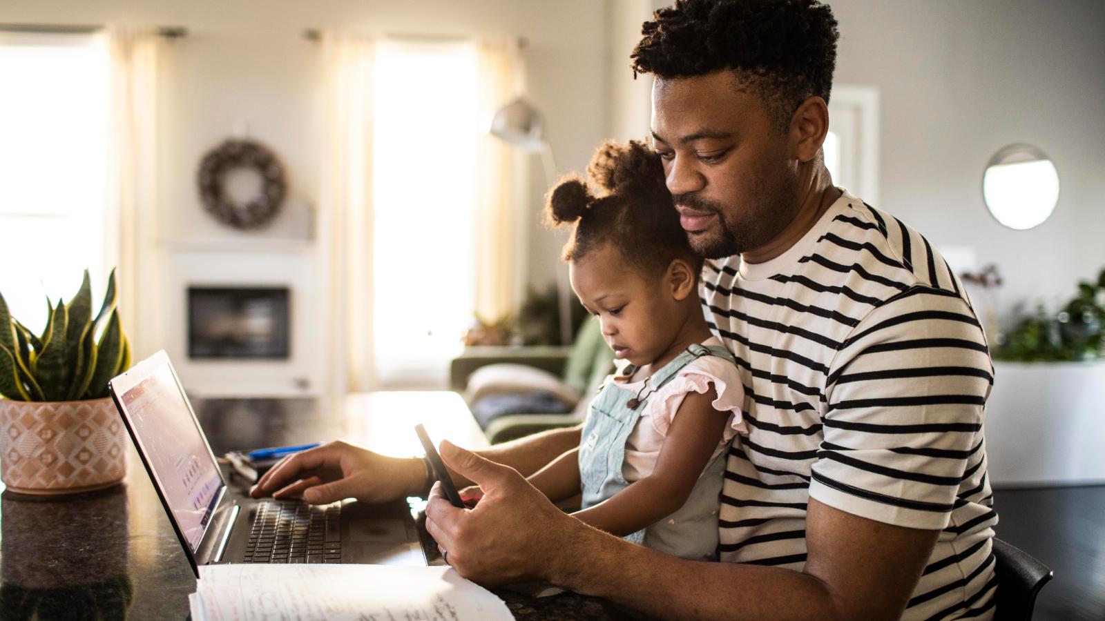 Father working from home while holding toddler