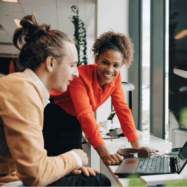 Smiling business woman leaning on her desk talking to her co-worker
