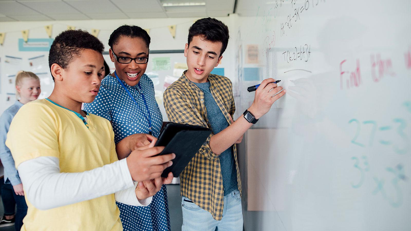 Two students with their teacher working on a problem at the white board.