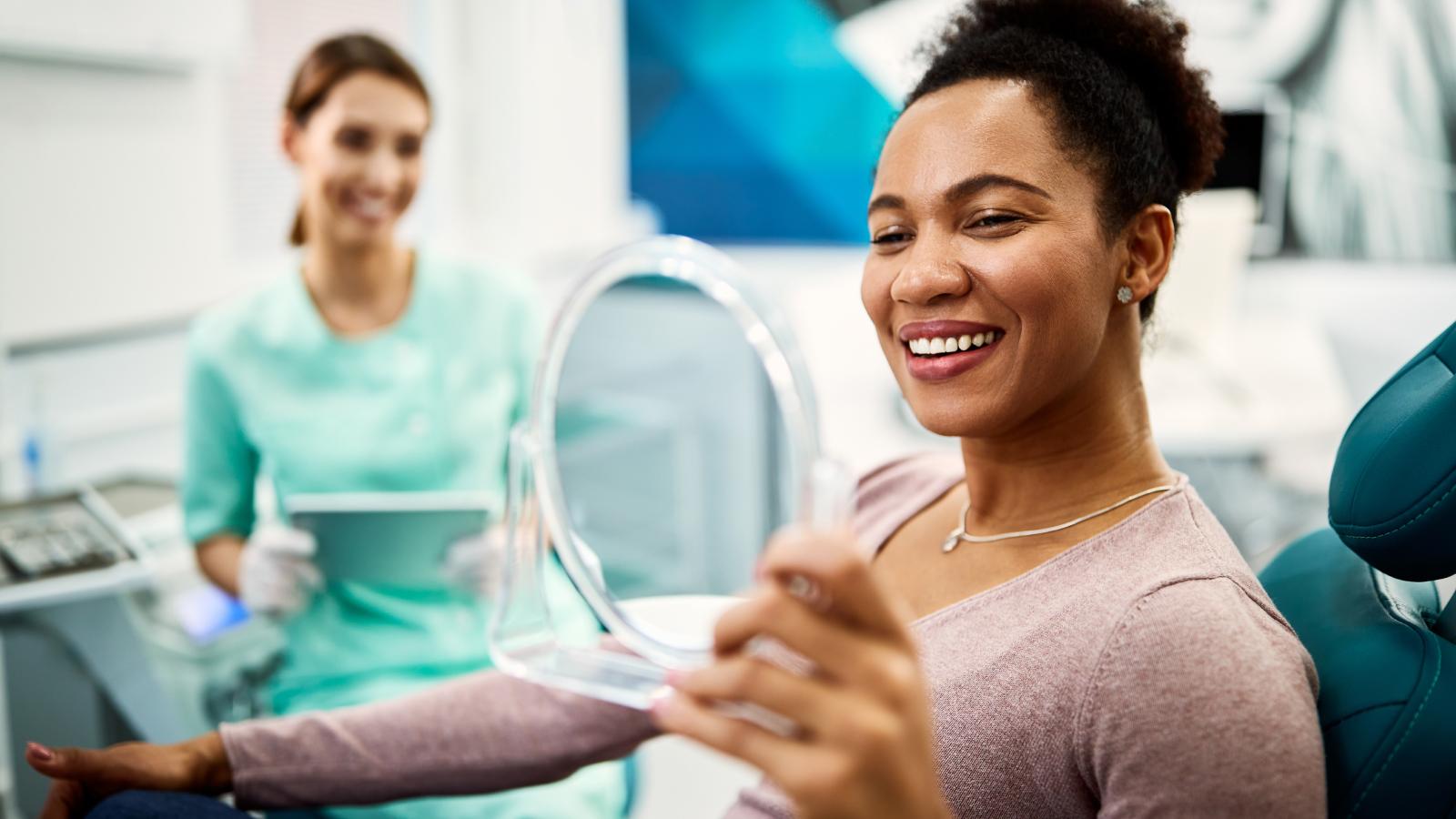 Woman holding a mirror and smiling in dentist office