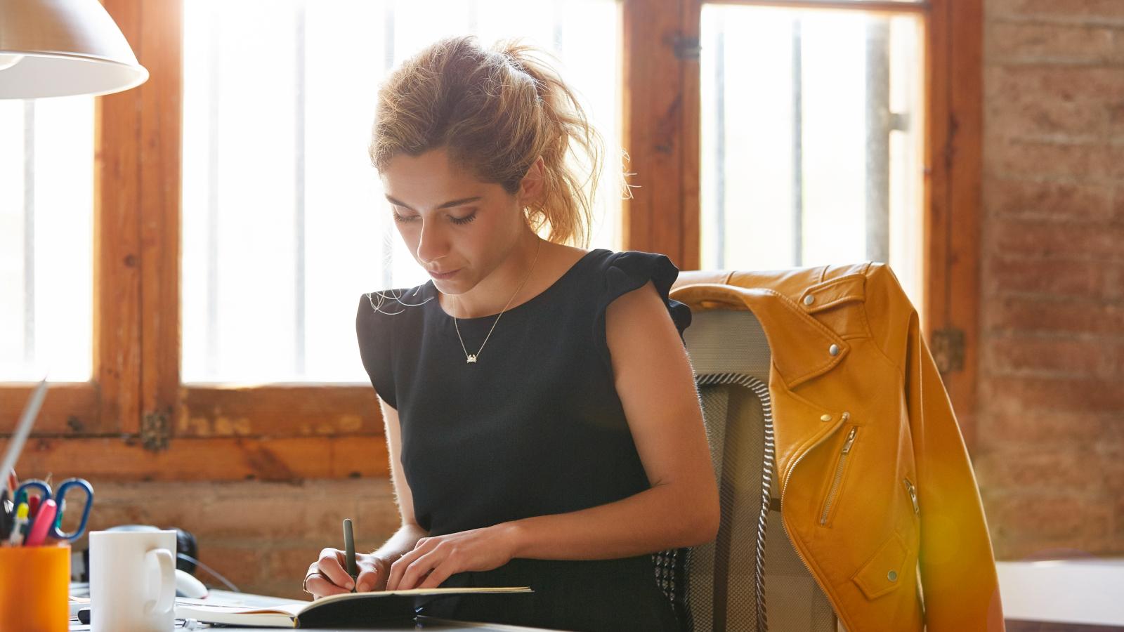 Businesswoman writing in book at desk