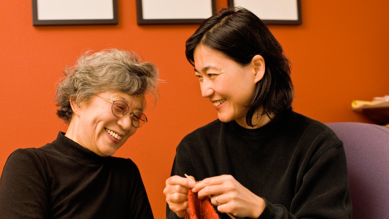Mother and her adult daughter smiling together at home.