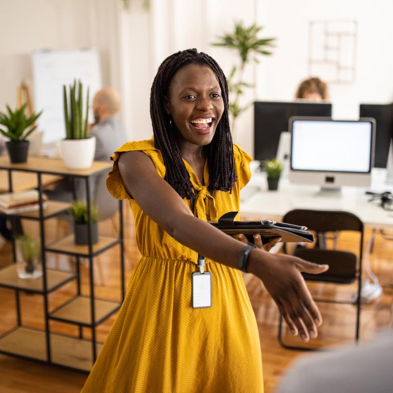A woman in a yellow dress welcomes a visitor to her office with a handshake