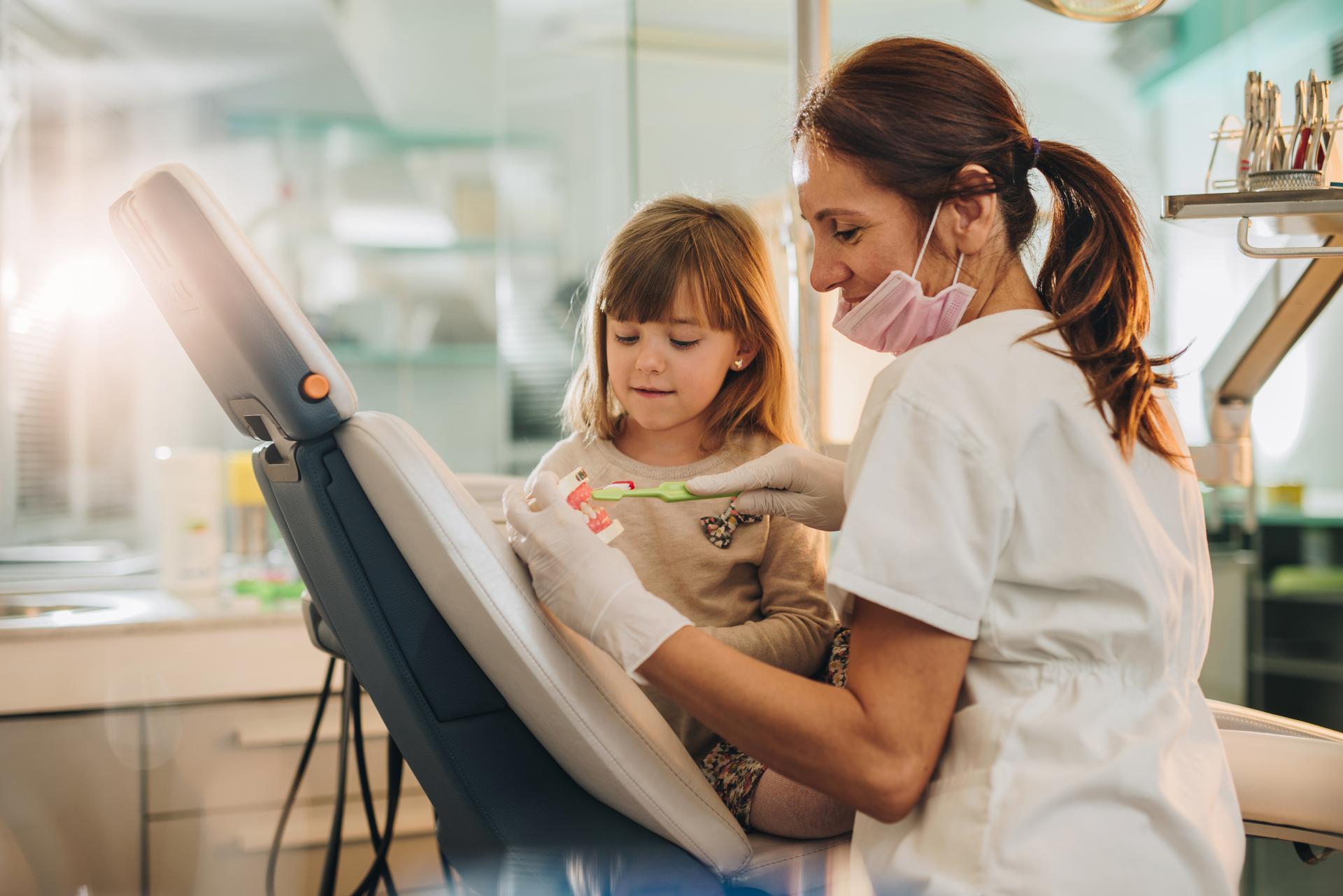 Little girl learning how to brush her teeth at dentist's office