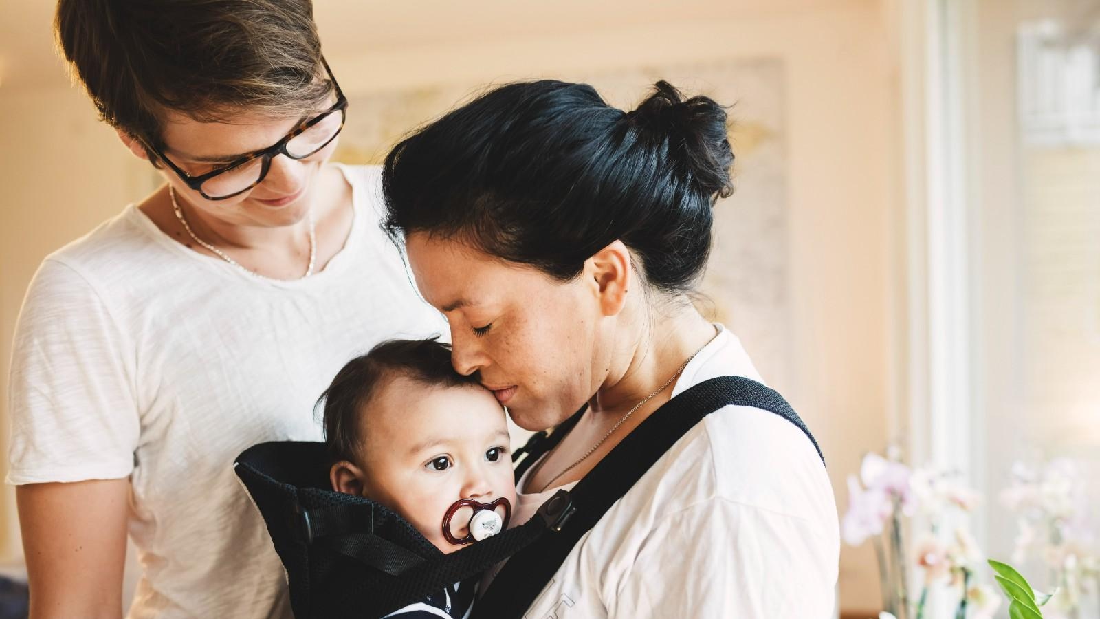 woman holding and kissing her baby while another woman looks at the baby