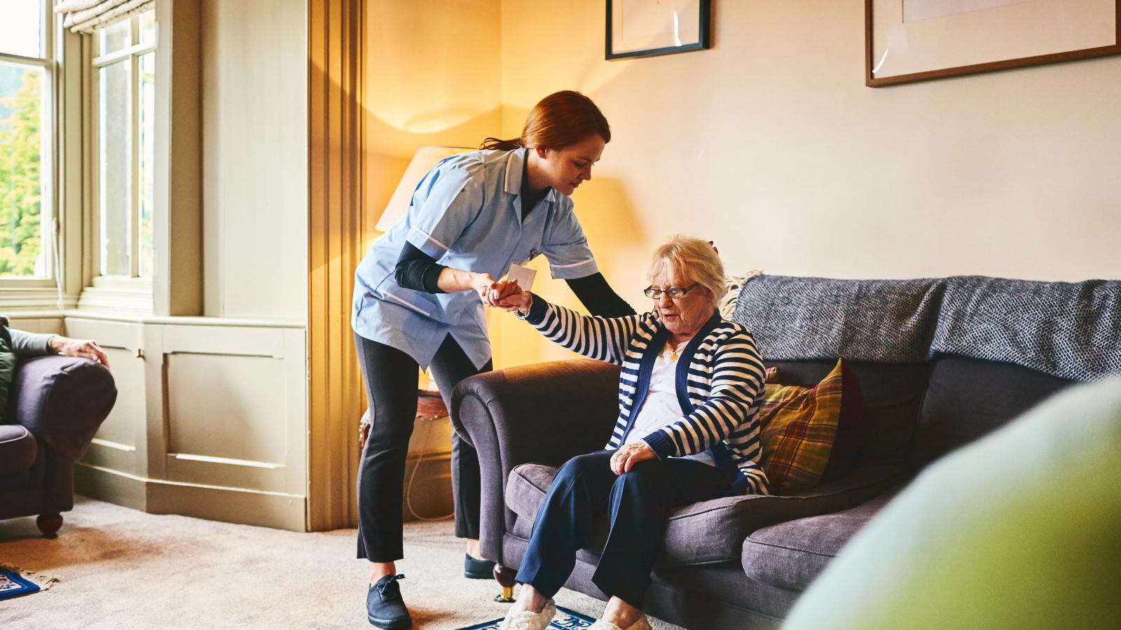 Professional caregiver helping an older woman stand up from a couch. Professional caregiver helping an older woman stand up from a couch.