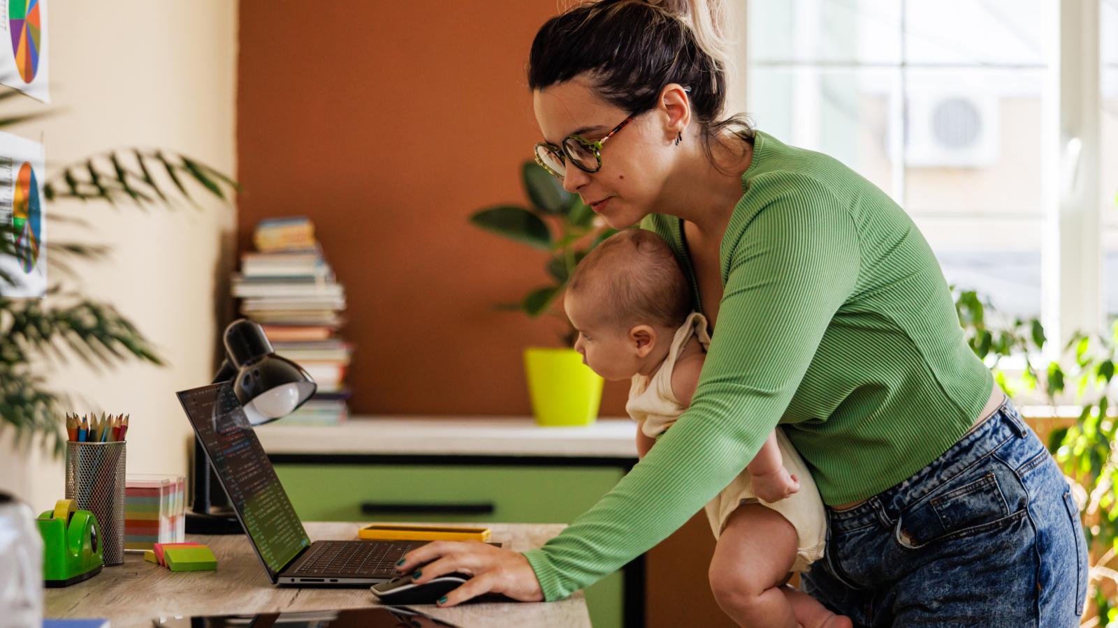 Mother holding child in arms and working on laptop