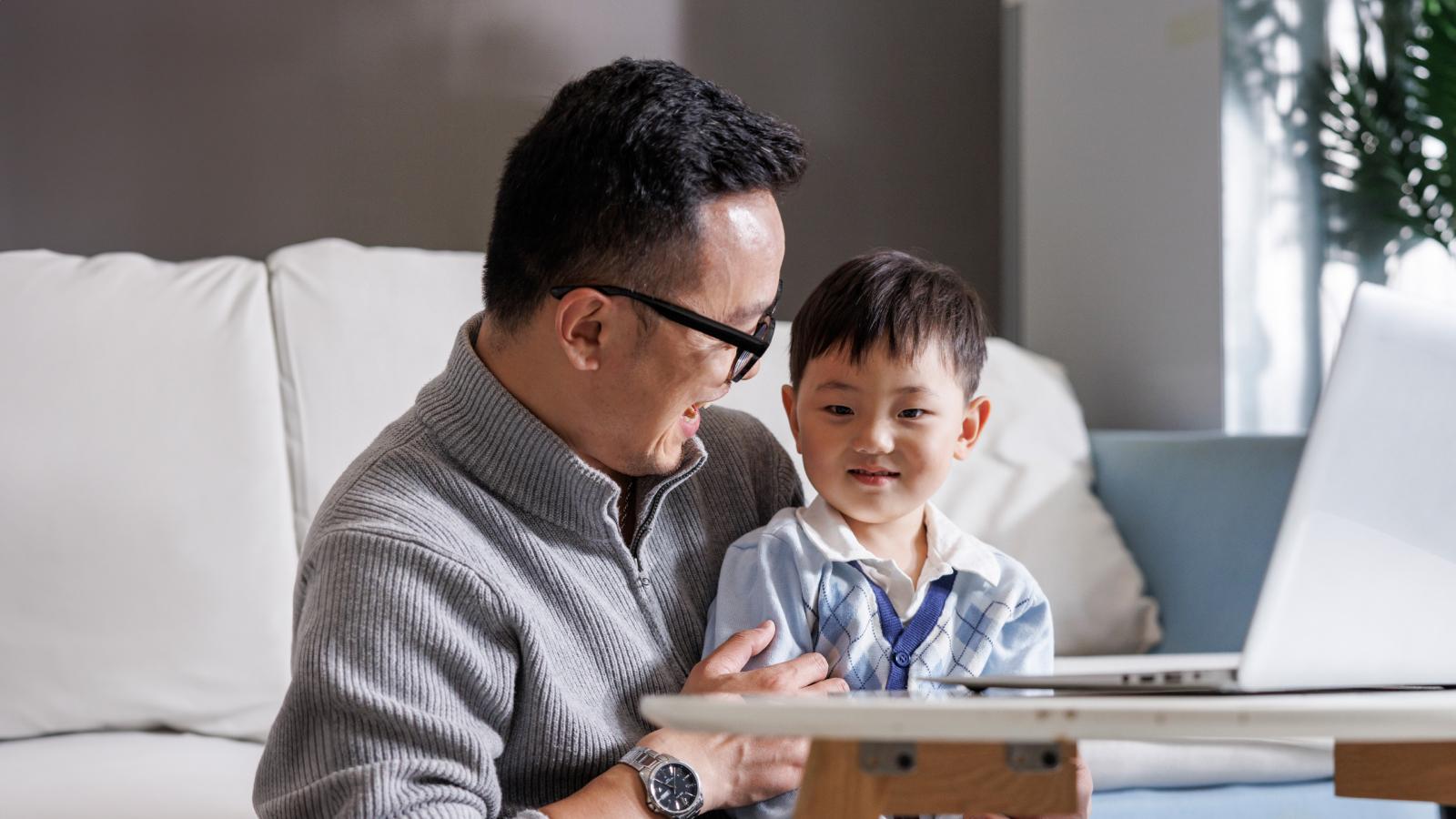 Father holding his son on his lap while working on his laptop