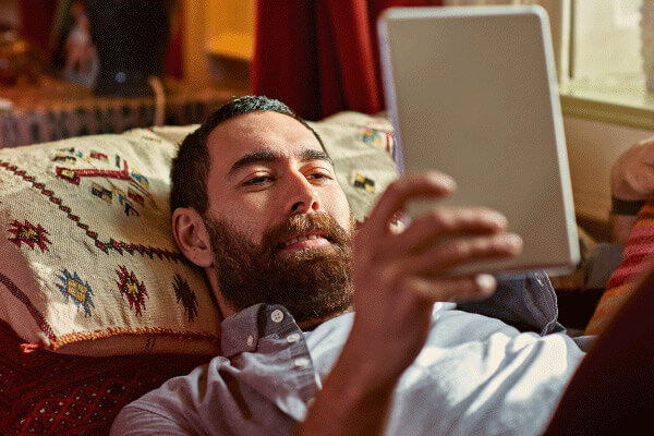 Man laying on his couch looking at his tablet