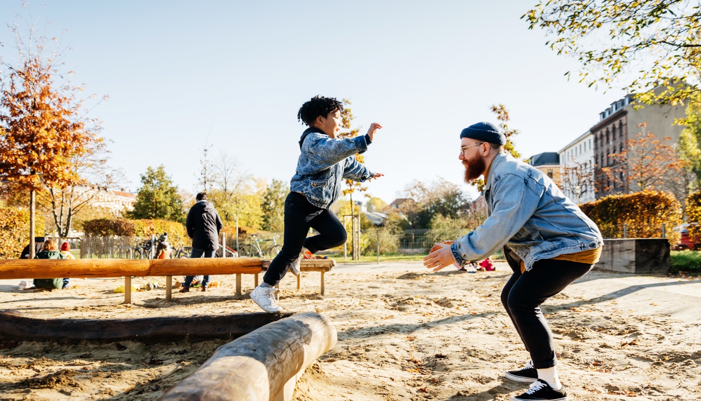 Father and child playing outside. The child is jumping toward the father.