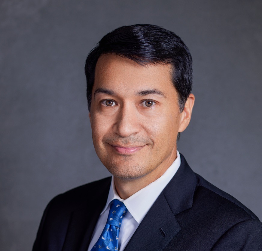 Michael Ferik smiles sweetly in a black suit jacket, white shirt, and a blue tie patterned with little baby animals. His dark hair rises slightly in the center.